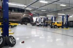 The interior view of the Shade Tree Auto garage with high ceilings, white floors, and 6-8 cars on blue lifts getting worked on by Shade Tree Auto technicians.